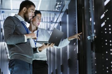 Two IT technicians standing in a server room in front of the racks reviewing and discussing something